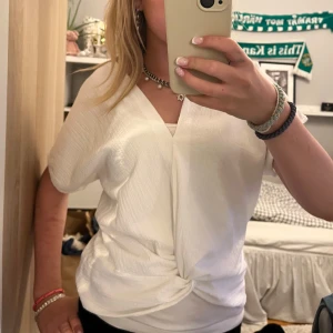 Vit omlottopp med knutdetalj - Säljer en vit omlottopp med snygg knutdetalj framtill och v-ringning. Toppen har korta ärmar och är gjord i ett lätt, strukturerat tyg som känns luftigt❣️