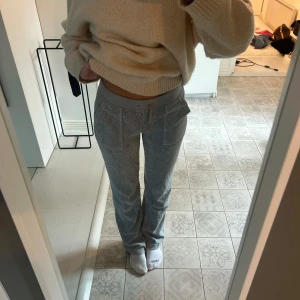 Grå mjukisbyxor från Juicy Couture - Säljer ett par grå mjukisbyxor från Juicy Couture med raka ben. Byxorna har bred resår i midjan med snörning, stora fickor fram och bakfickor med knappdetaljer. Perfekta för chill dagar eller när du vill vara bekväm men ändå se snygg ut. Inga märken av användning😊😊😊💖💖