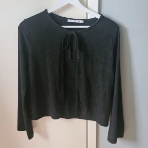 Svart långärmad topp med knyt - En svart långärmad topp från 157 med rund halsringning och snygg knytning framtill. Enkel och stilren design som passar perfekt till jeans eller kjol. Mjuk och skön känsla, perfekt för dig som gillar minimalistiska plagg.