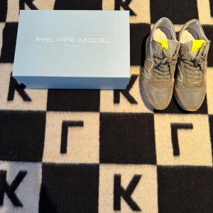 Philippe model skor  - Snygga sneakers från Philippe Model i grå mocka och textil med coola neon-gula detaljer på plös och sula. Skorna har snörning och en klassisk sportig siluett, perfekt för dig som gillar streetstyle och vill sticka ut lite extra.
