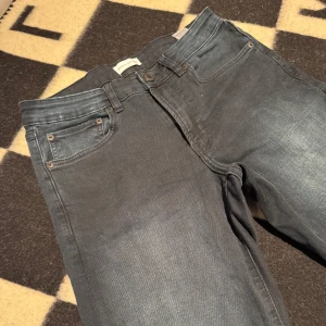 Mörkgrå jeansbyxor i slim fit 30/30 - Snygga mörkgrå jeansbyxor med klassisk femficksdesign och smal passform. Jeansen har en lätt tvättad look och raka ben. Perfekta för dig som gillar en stilren och enkel vibe. Materialet är mjukt och stretchigt för extra komfort.