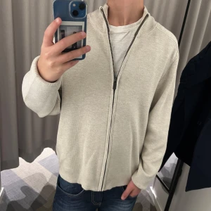 Beige kofta med dragkedja - Snygg beige kofta med hel dragkedja framtill. Tröjan har en enkel och stilren design med långärmade ärmar och ribbade muddar. Perfekt för lager-på-lager och passar till både jeans och t-shirt.