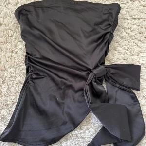 Topp i skinnimitation  - Snygg bandeau/tubtopp i skinnimitation med rosett. ❤️Har dragkedja på sidan för att lättare få på sig den samt gummi längst upp så den inte åker ner. Aldrig använt med prislapp kvar, men tyvärr från shein. Perfekt till fest! 