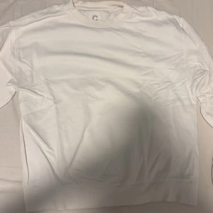 Vit sweatshirt från C - Säljer en stilren vit sweatshirt från C med rund hals och ribbade muddar. Tröjan är enkel och clean, perfekt för dig som gillar minimalistisk stil. Materialet känns mjukt och skönt mot huden, och den har lång ärm. Passar dig som vill ha en basic tröja i garderoben.