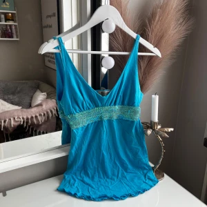 Turkos paljettopp från Illucious - Snygg turkos linnetopp i storlek M, men passar mig som vanligtvis är XS  från Illucious med smala axelband och v-ringning. Toppen har ett brett band med glittrande paljetter under bysten som ger extra bling. Perfekt för dig som vill sticka ut med färg och detaljer. Mjuk och skön bomullskänsla. 