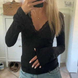 Svart långärmad topp med spets - Säljer en svart långärmad topp med v-ringning och fina spetsdetaljer längs halsringningen, lite utsvängda ärmar. Aldrig använd.💕