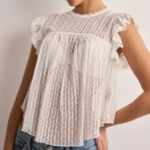 Svart spetsblus med volang från Nelly - Supersöt svart blus från Nelly i transparent spets med volangdetaljer vid ärmarna och knytning i nacken. Blusen har korta ärmar och ett luftigt, flowy fall. Perfekt att styla med jeans eller kjol för en trendig look.