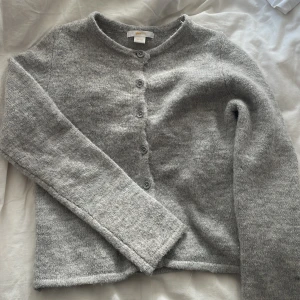 Grå stickad kofta från Gina Tricot - Mysig grå stickad kofta från Gina Tricot i storlek 134/140. Nästan helt oanvänd. Ser ut som en ny. 