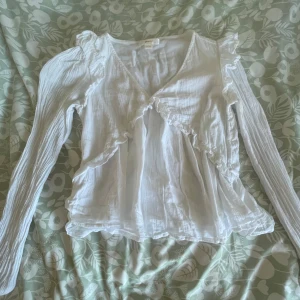 Vit volangblus med v-ringning från Ginatricot - Supersöt vit blus med v-ringning och volangdetaljer längs bröstet och axlarna. Långa ärmar med lätt rynk och flowig passform. Perfekt för dig som gillar romantisk och luftig stil. Tunt, mjukt tyg som känns skönt mot huden. Nästan aldrig använd och pris kan diskuteras. Den är i storlek 146-152