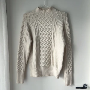Cremevit stickad tröja från Vero Moda - Säljer en creme vit stickad tröja från Vero Moda i storlek S. Tröjan har ett snyggt flätmönster framtill och på ärmarna, samt en ribbad hög krage och muddar. Perfekt för dig som gillar mysiga och stilrena plagg med lite extra struktur.