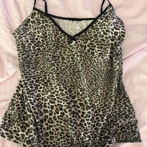 Leopardmönstrad linnetopp med smala band - Snygg linnetopp med leopardmönster och tunna svarta axelband. Toppen har v-ringning med svart kant och en liten rosett framtill. Perfekt för dig som vill sticka ut med ett djurmönstrat plagg.