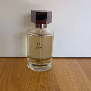 Zara Bye Love Eau de Parfum - Fräsch parfym från Zara med namnet Bye Love. Flaskan är cylindrisk i genomskinligt glas med en ljusgul vätska och har ett stilrent, mörkgrått sexkantigt lock. Perfekt för dig som gillar minimalistisk design och vill ha en modern doft i samlingen.