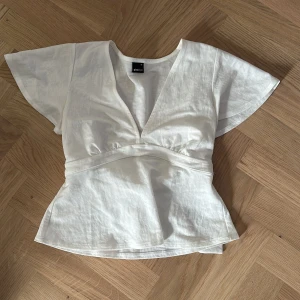 Vit omlottopp från Gina Tricot XS - Superfin vit omlottopp från Gina Tricot i storlek XS. Toppen har v-ringning, korta vida ärmar och knytband i midjan. 