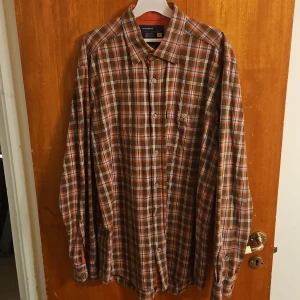 Rutig skjorta från Tonelli Collection L - Snygg rutig skjorta från Tonelli Collection i storlek L. Skjortan har bruna, orangea och vita rutor, klassisk krage och knäppning framtill. Tillverkad i 100% bomull och har en bröstficka. Perfekt för dig som gillar avslappnad stil.