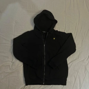 Svart zip hoodie från Lyle & Scott Junior - Svart hoodie från Lyle & Scott Junior med dragkedja. Tröjan har använt fåtal gånger och är i bra skick, bara något skrynklig då den luggat i gadderoben men bara att stryka så är den som ny!