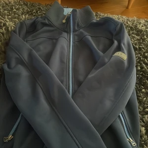 Blå softshelljacka från ANKY M - Mörkblå softshelljacka från ANKY med ljusblå dragkedja och ribbad krage. Insidan är fodrad med mjuk fleece och jackan har två fickor med dragkedja. Perfekt för dig som gillar sportig och clean stil. Är mestadels för riding. Det är själva Anky som har gjort modellen därför kostar den ca 1000 kr helt ny. Kan tänka mig sänka priset.