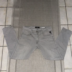 Grå slim fit jeans från Replay - Snygga grå jeans från Replay i modellen RIK med slim fit. Klassisk femficksdesign, raka ben och diskreta sömmar på bakfickorna. Jeansen är tillverkade i mjukt denimtyg och passar perfekt till en avslappnad streetstil.
