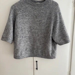 Grå stickad tröja med tre kvarts ärm - Mysig grå stickad tröja med korta ärmar och rund halsringning. Tröjan har en avslappnad passform och är perfekt för lager-på-lager. Enkel och stilren design som funkar till många olika looks.