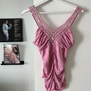 Rosa paljettprydd linnetopp - Säljer en ljusrosa linnetopp med glittriga paljetter och broderad mesh i V-ringning. Toppen har rynkade detaljer framtill och smala axelband. Materialet känns mjukt och lätt, perfekt för att sticka ut med extra bling. Supersnygg till svarta byxor eller jeans!