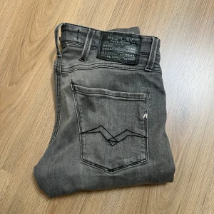 Replay Anbass grå  - Snygga Replay Anbass jeans i grå tvätt med slim fit passform. Klassisk femficksdesign, svarta detaljer och coola broderier på bakfickorna. Jeansen har knapp och dragkedja framtill samt Replay-logga på fickan. Perfekta för dig som gillar stilrena och moderna jeans. Passar mig perfekt och jag är 180cm lång och väger stax under 50kg. Jeansen har en lagning på högra bakfickan men det är inget man tänker på. Hör av dig vid mista fundering. Priset är inte hugget i sten👑