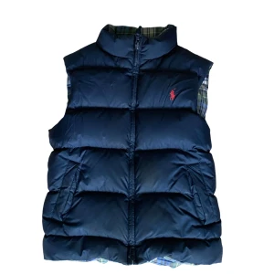 Blå dunväst från Polo Ralph Lauren - Snygg blå dunväst från Polo Ralph Lauren med röd logga på bröstet. Västen är vändbar med ena sidan i marinblått och andra sidan i blågrön rutig med broderat emblem och stor siffra 2 på ryggen. Ungefär storlek 164