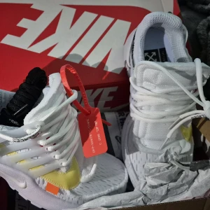 Nike Presto Off-White sneakers vit/gul - Nike Presto Off-White sneakers i vitt med detaljer i gult och svart. Snygg design med textprint, genomskinliga paneler och klassisk Off-White zip-tie i rött. Skorna har snörning, platt sula och rund tå. Materialet är syntet och mesh för en skön känsla.