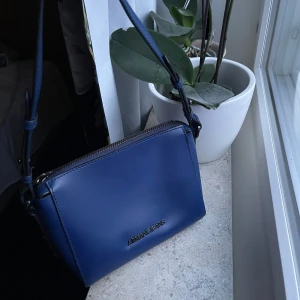 Blå axelväska från Armani Jeans - Snygg blå axelväska från Armani Jeans  med silverfärgad logga framtill. Väskan har justerbar axelrem och dragkedja upptill. Insidan är mönstrat  i vitt, blå och svart. Perfekt storlek för det viktigaste.Helt ny