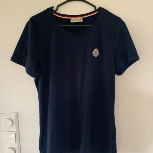 Marinblå Moncler t-shirt i bomull - Snygg marinblå t-shirt från Moncler med klassisk rund hals och  logga på bröstet. Tillverkad i mjuk bomull och har korta ärmar. Köpt second hand men i väldigt bra skick! Hör av er om ni har frågor eller vill ha mer bilder🤗
