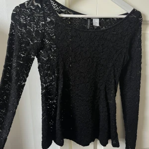 Svart spetsblus från Divided - Säljer en svart långärmad blus från Divided med genombruten spets och blommigt mönster. Toppen har rund halsringning och sitter snyggt på kroppen. Perfekt för dig som vill ha en stilren men ändå cool look.