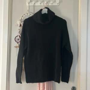 Svart stickad polotröja - Mysig svart stickad polotröja med bred, ribbad krage och långa ärmar. Tröjan har en relaxed fit och ribbade muddar vid ärmslut och nederkant. Perfekt för lager-på-lager under kyliga dagar.