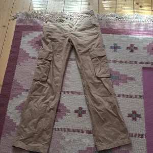 Beige cargopants  - Snygga beige cargopants med raka ben och flera stora fickor på sidorna. Byxorna har klassisk cargostil och är tillverkade i bomull för en skön känsla. Perfekta för dig som gillar en avslappnad och praktisk look.