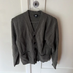 Grå kofta från Uniqlo XS - Mysig grå kofta från Uniqlo i storlek XS. Klassisk modell med v-ringning, knappar framtill och två fickor. Tillverkad i mjukt stickat material, perfekt att slänga på sig över en t-shirt eller skjorta. Enkel och stilren design som funkar till det mesta. Priset är diskuterbart