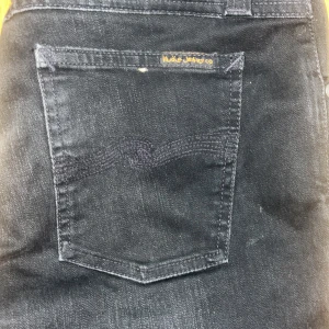 Svarta jeans från Nudie Jeans - Svarta jeans från Nudie Jeans med klassisk femficksdesign och diskret broderad bakficka. Jeansen har en smal passform och är tillverkade i mjukt denimtyg. Perfekta för dig som gillar stilrena och tidlösa plagg. Modellen är skinny lin storlek w30 l32