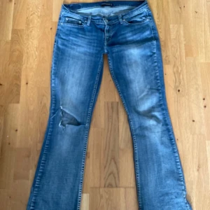 low waisted bootcut  - Snygga Levis 527 Superlow jeans i klassisk blå tvätt med slitningar och bootcut-ben. Låg midja och femficksmodell, tillverkade i mjukt jeanstyg. Perfekta för dig som gillar en avslappnad och retro vibe. jag är M som preferens och ja passar i de men lite lite lösa i midjan. uppskattar till 38/40