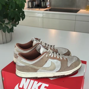 Nike Dunk Low Retro medium curry - Nike Dunk Low Retro medium curry sneakers i snygga beige och bruna toner. Ovandel i mocka och skinn med vita detaljer och klassisk Swoosh. Låg modell med platt sula och rund tå. 
