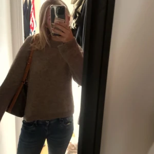 Beige stickad tröja i loose fit - Mysig beige stickad tröja med rund hals och lång ärm. Tröjan har en enkel och stilren design med lite lösare passform, perfekt att slänga på sig till jeans. Materialet känns mjukt och skönt mot huden.