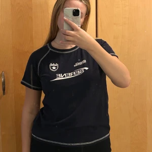 Mörkblå SERENE t-shirt med kontrastsömmar - Mörkblå t-shirt med vita kontrastsömmar och tryck framtill med texten 'EMBRACE THE FUTURE' och ett stjärn-emblem. Klassisk rund hals och korta ärmar. Skön passform och sportig vibe, perfekt till jeans eller shorts.