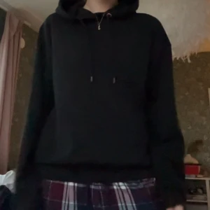 Svart hoodie med huva och snörning - En klassisk svart hoodie med huva och snörning. Tröjan har en relaxed passform, långa ärmar och ribbade muddar vid ärmslut och nederkant. Perfekt för chill dagar eller när du vill ha en enkel och stilren look. Använd fåtal gånger!