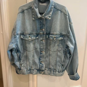 Oversized ljusblå jeansjacka - Säljer en oversized ljusblå jeansjacka med klassisk krage och silverfärgade knappar. Jackan har två bröstfickor med lock och knapp, samt långa ärmar. Perfekt att slänga över en t-shirt för en chill look.