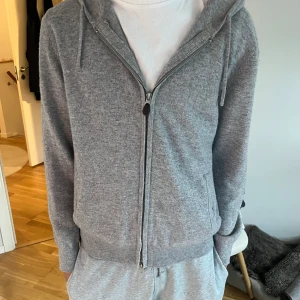 Grå hoodie i kashmir från SayLess - Snygg grå hoodie från SayLess i mjuk kashmir. Tröjan har huva med snörning, dragkedja framtill och ribbade muddar. Perfekt för chill dagar och har en clean look som funkar till allt. Passformen är normal och materialet är riktigt lyxigt.