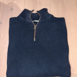 Mörkblå stickad half zip-tröja Zara - Mörkblå stickad tröja från Zara med grov ribbstickning och en snygg half zip-dragkedja vid halsen. Tröjan har hög krage och långa ärmar, perfekt för lager-på-lager under kyliga dagar.