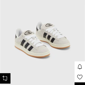 Adidas Campus sneakers i mocka - Snygga Adidas Campus sneakers i ljusgrå mocka med klassiska svarta ränder på sidorna och vit sula med gummidetalj. Skorna har rund tå, platt sula och vit snörning. Perfekta för dig som gillar retrostil och vill ha något som funkar till jeans och hoodie.