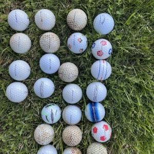 golfbollar - Bilden visar flera golfbollar av olika märken och skick, utlagda på gräs. Ingen bok syns på bilden.