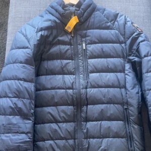 Blå dunjacka från Parajumpers - Säljer en blå dunjacka från Parajumpers med klassisk patch på ärmen och dragkedjor framtill. Jackan har lång ärm och quiltad design som ger en sportig look. Perfekt för kyliga dagar och enkel att matcha med olika outfits.