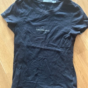 Svart t-shirt från Calvin Klein Jeans - Svart t-shirt från Calvin Klein Jeans med vit logga tryckt på bröstet. Klassisk rund halsringning och korta ärmar. Perfekt basplagg med enkel och stilren design.