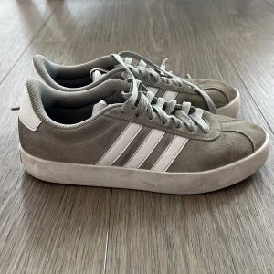 Grå Adidas sneakers - Säljer ett par grå sneakers från Adidas med klassiska vita ränder på sidorna. Skora har använts och säljer för de är för små. Hör av dig om du är intresserad.