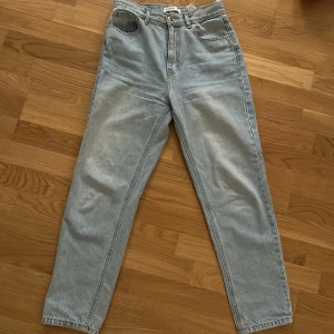 Ljusblå högmidjade jeans - Säljer ett par klassiska ljusblå jeans med hög midja och raka ben. Jeansen har fem fickor och stängs med dragkedja och knapp. Perfekta till vardags och lätta att matcha med olika toppar.