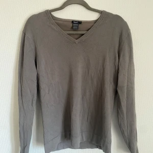Mörk Beige tröja från Filippa K - Säljer en stilren mörk beige tröja från Filippa K. Tröjan har en v-ringad design och är tillverkad i en mjuk bomullsblandning. Perfekt för en avslappnad och snygg look.