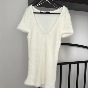 Vit fluffig topp med v-ringning från BikBok - Supersöt vit topp från BikBok i fluffigt material. Djup v-ringning och korta ärmar ger en trendig look. Perfekt för dig som vill sticka ut med en mysig och stilren outfit.