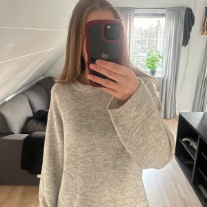 Ljusgrå stickad tröja - Mysig ljusgrå stickad tröja med rund halsringning och långa ärmar. Tröjan har en enkel och stilren design, perfekt för lager-på-lager och passar till många olika outfits.